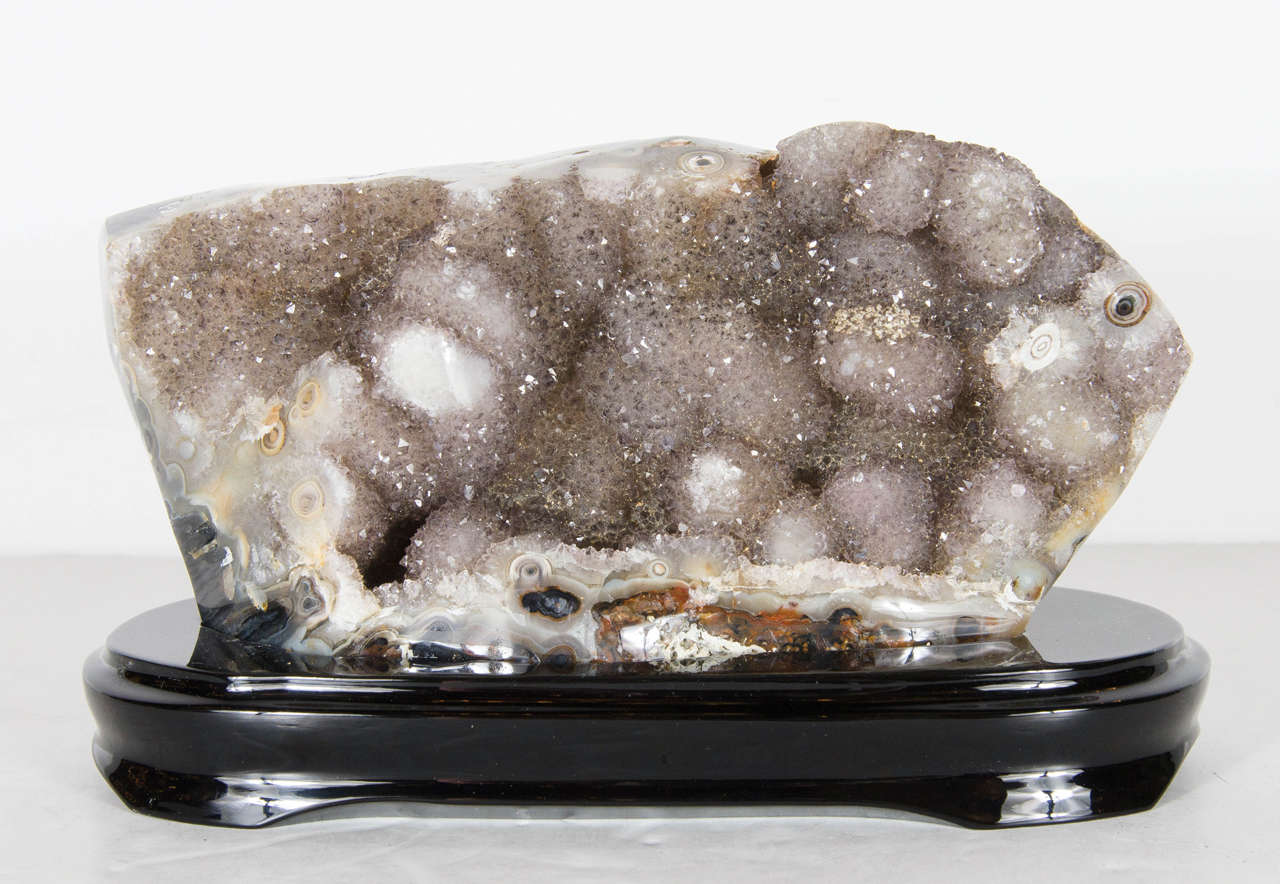 This captivating geode crystal specimen features myriad shades of smokey crystalline geode. It offers a beautiful shape, and free stands on a custom ebonized walnut base. It would be a stunning addition to any interior, from domestic to corporate,