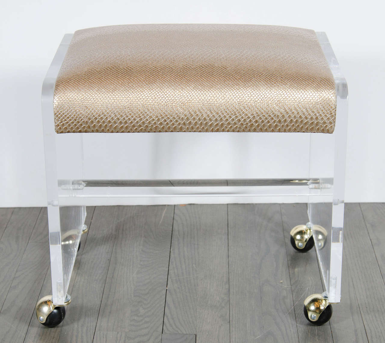 This chic Mid-Century Modernist Lucite stool features an open cube-like form with castors and brass covers, one thick Lucite support rod and a comfortable seat newly upholstered in faux bronze python that rests between the Lucite side supports with