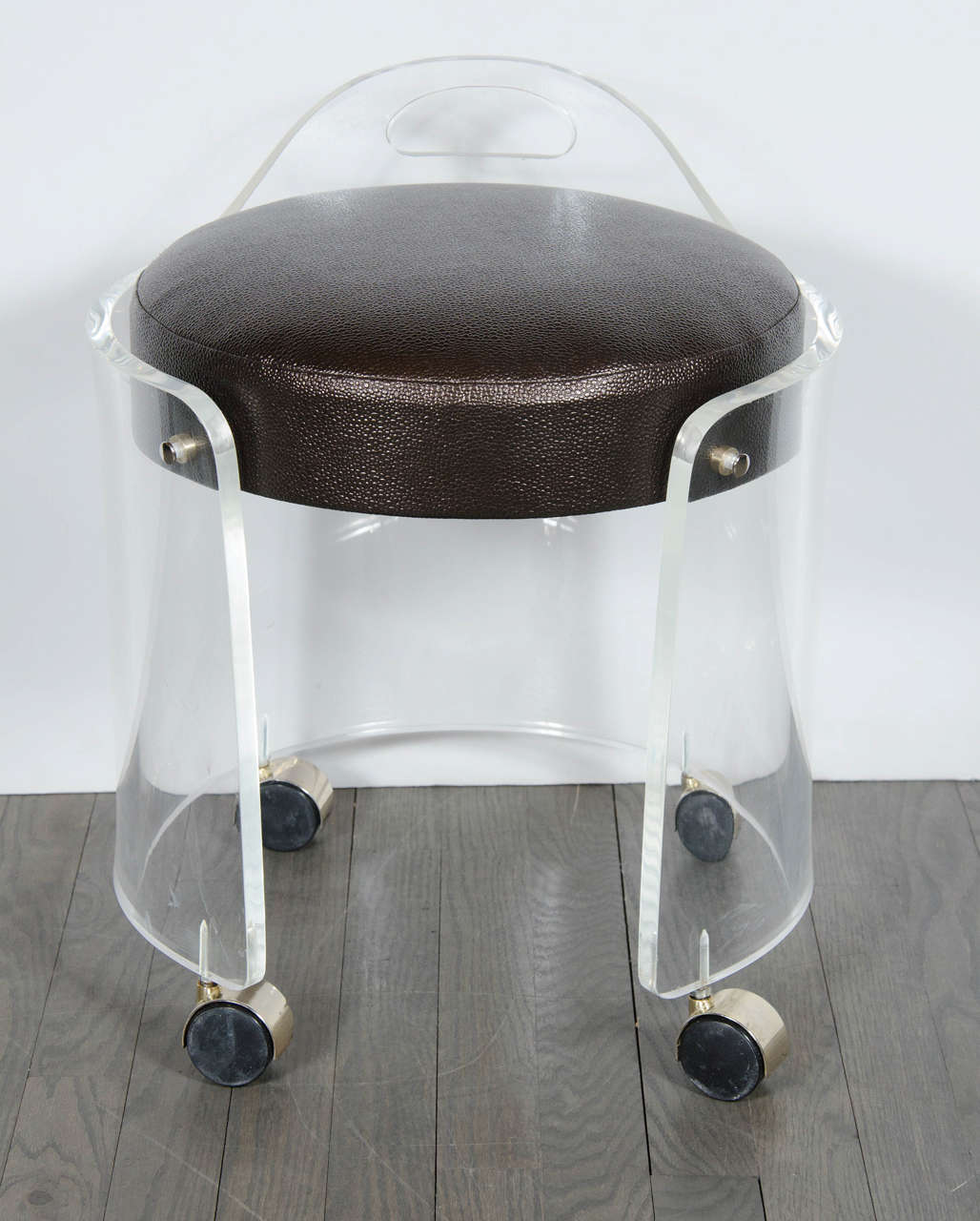 This chic Mid-Century Modernist round Lucite stool features a curved form with an open Front Design, four castors with brass covers and a comfortable seat newly upholstered in faux bronze shagreen that rests just inside the curved Lucite side