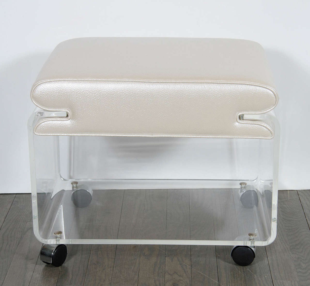 This chic Mid-Century Modernist enclosed waterfall form Lucite stool features an open cube-like form on castors with chrome covers and a comfortable seat newly upholstered in faux oyster shagreen that rests between the open ended Lucite side