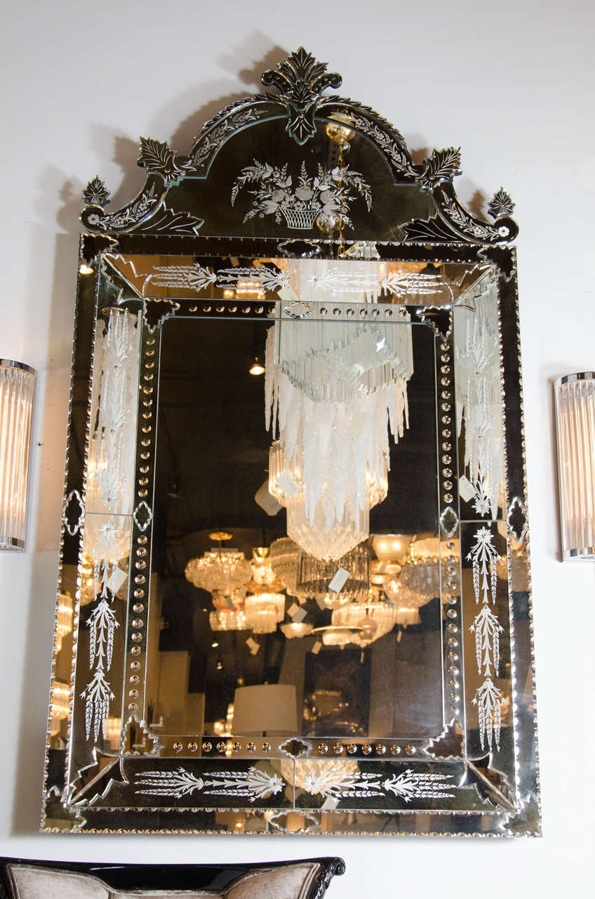 This rare Venetian style mirror features hand beveled and reversed etched floral and stylized foliage detailing. A gorgeous scroll form pediment detail crowns this gorgeous mirror. The detailing on this mirror is stunning, and is quite a statement