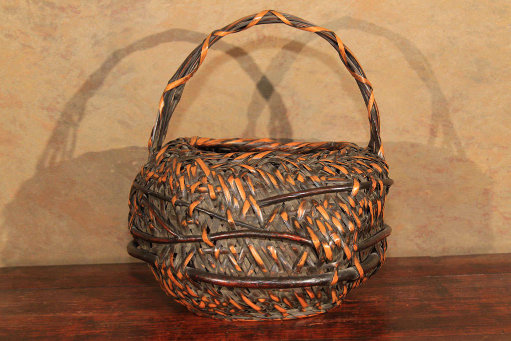 Japanese hanakago flower basket for use in ikebana, the art of flower arrangement. The irregular shaped body of the basket woven of aged and split bamboo, interwoven with cherry (sakura) branches. With a sweeping overhead handle of wrapped bamboo.