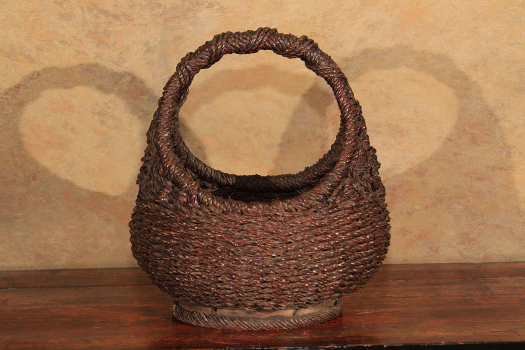 Japanese rope braid ikebana basket used in the art of flower arrangement. Made of split and dyed woven bamboo and reed. With a graceful hurdle form handle and rounded oblong body. With an unrecorded signature on the base of the basket.