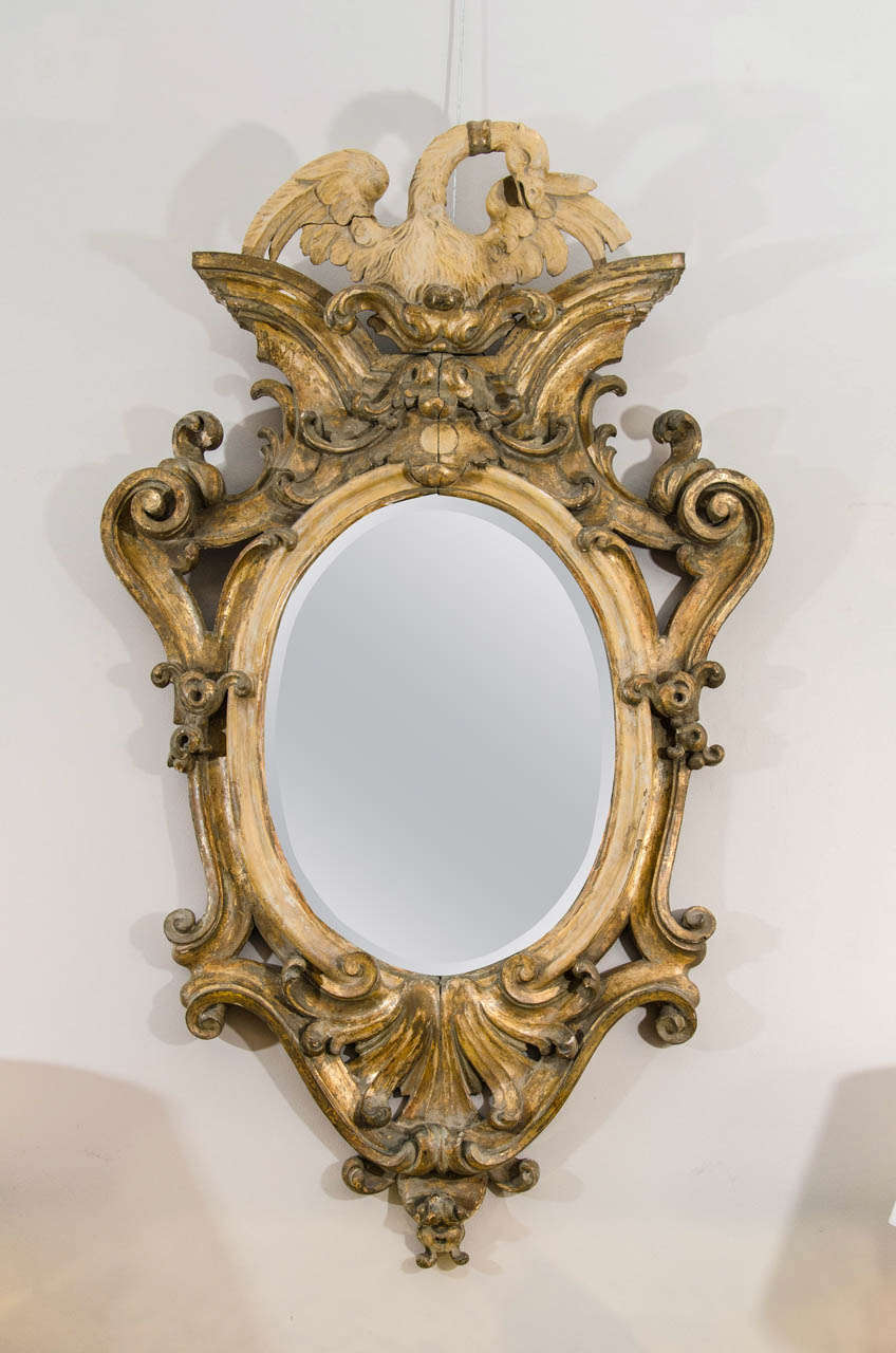 The oval mirror with carved and gilded cartouche form frame with a painted swan on cresting.