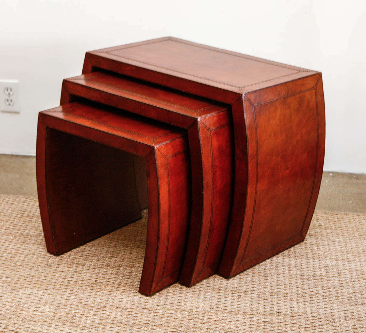In a gorgeous cognac leather, this set of three nesting tables with contrast stitching are distinctive and sophisticated. They're lovely as a trio, of course, but work equally well when split apart to be used individually. The sides are slightly