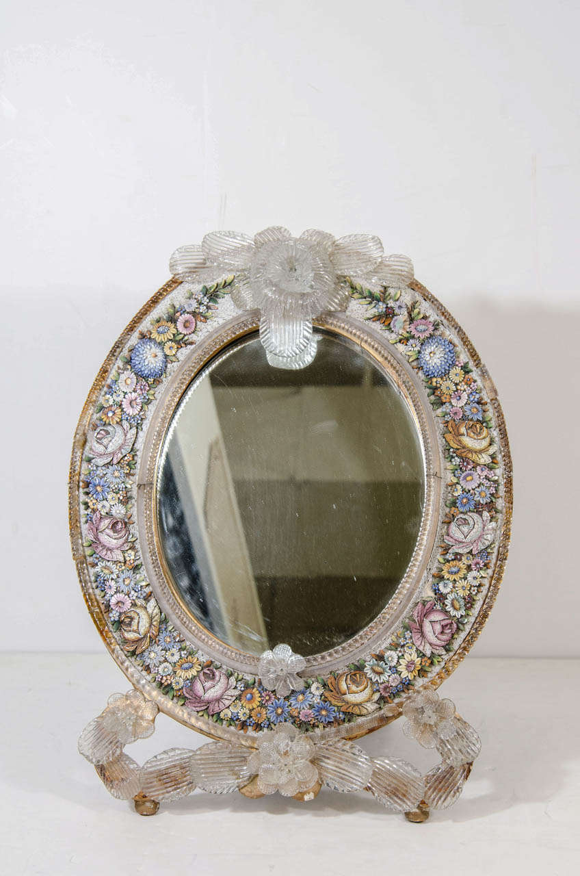 An antique Venetian table mirror with colorful micro mosaic floral design and glass flowers adorning the top and bottom of the mirror.

Good condition with age appropriate. Some loss to the micro mosaic