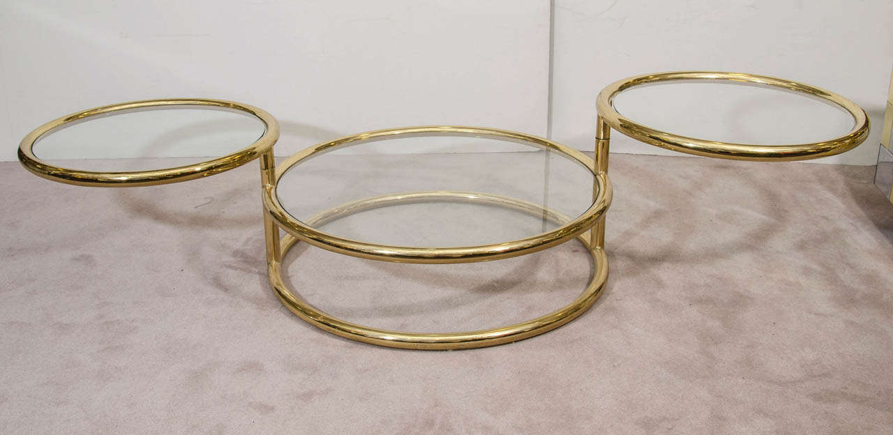 A vintage three tier brass swivel table in the style of Milo Baughman.  The top two tiers of this versatile table pivot to expand to a width of 73.5 inches.  It can function as a side table when closed or a coffee table when fully open.  Glass has a