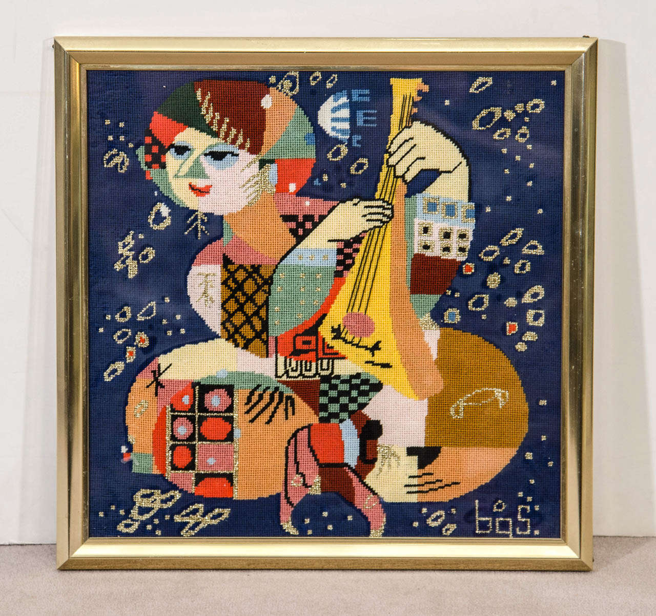 A vintage Wiinblad inspired needlepoint in a brass and glass frame depicting a musician. Good vintage condition with age appropriate wear.