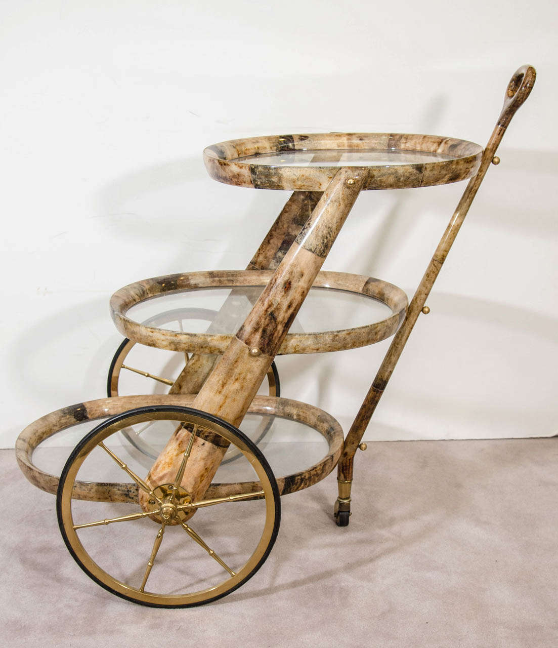 A vintage Italian Aldo Tura patchwork style lacquered goatskin bar cart with three glass top oval tiers and brass spoked wheels.

Tiers: 
Top: 30" H X 19" D X 17" W.
Middle: 19" H X 22" D X 17" W.
Bottom: 8" H