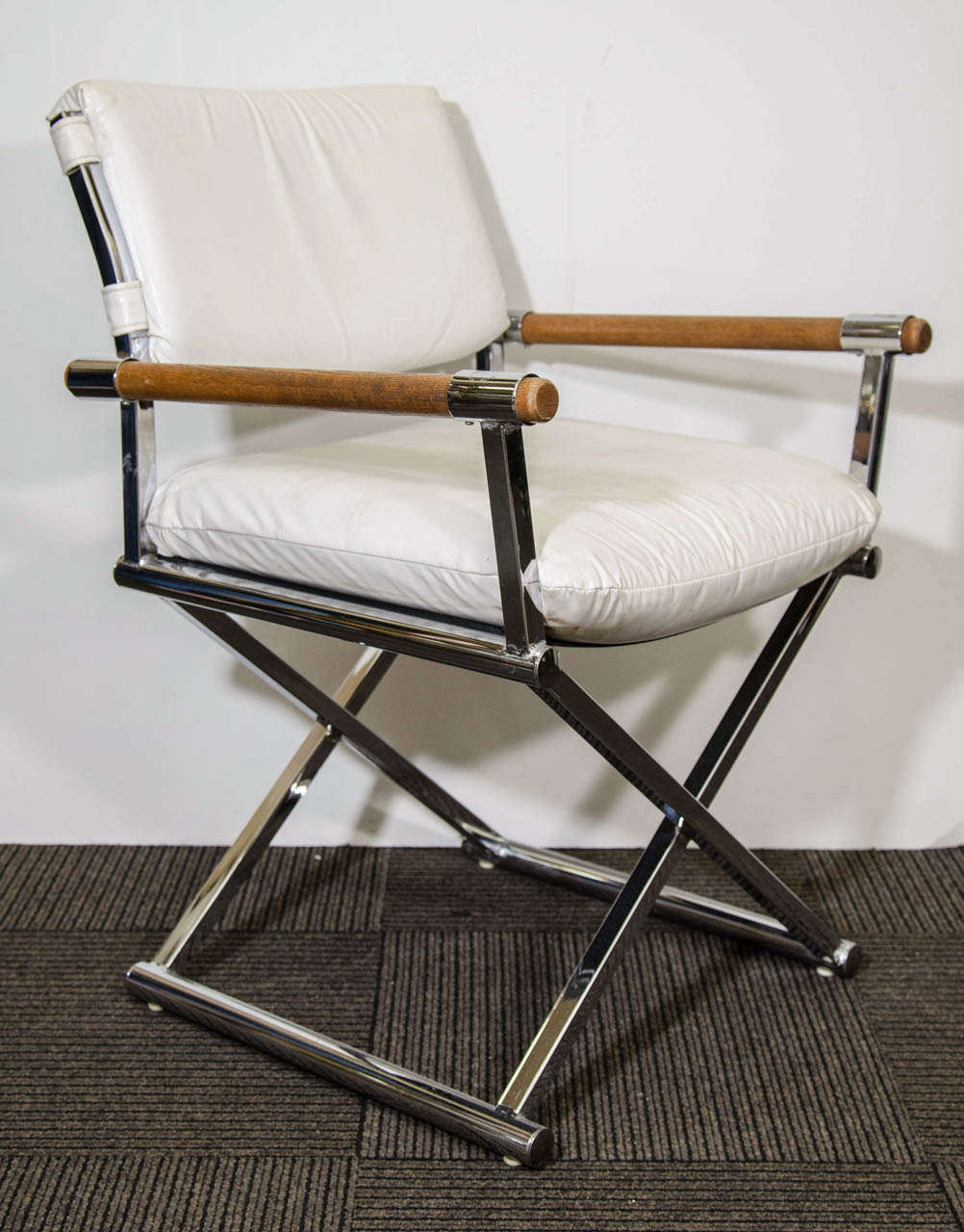 A pair of vintage director's chairs in white leather with a metal x-base frame and wooden arm rests. 

In good vintage condition with age appropriate wear. Some discoloration and scratches to the wood, small dents and scratches to metal, and a few