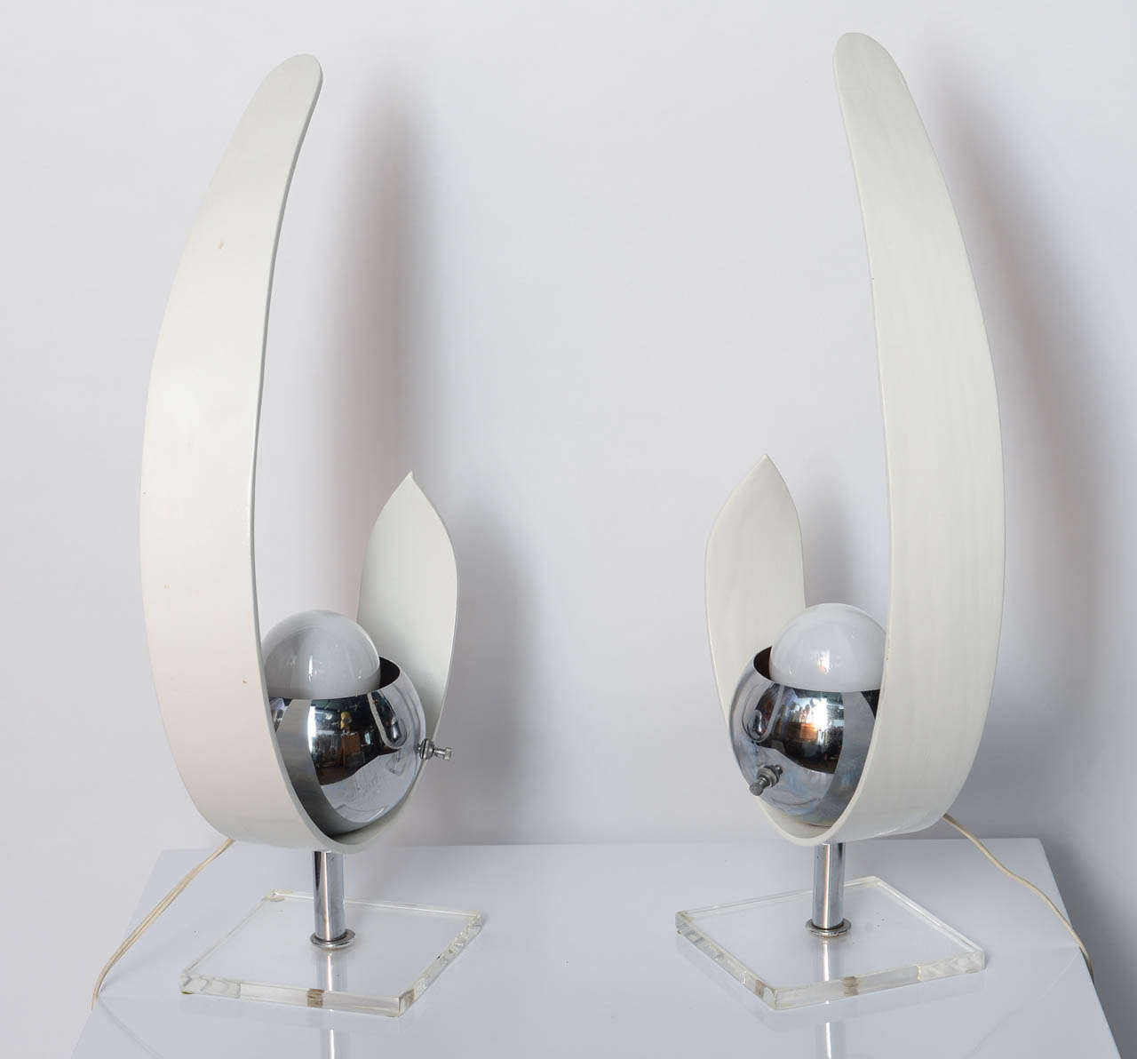 This 1960s Modernist Robert Sonneman Style Wood and Chrome Eyeball Table Lamps will bring a pretty Mid-Century touch on any furniture.
Each lamp has a metal switch on chrome bowl and has a clear acrylic base.  
The white lacquered can be lacquered