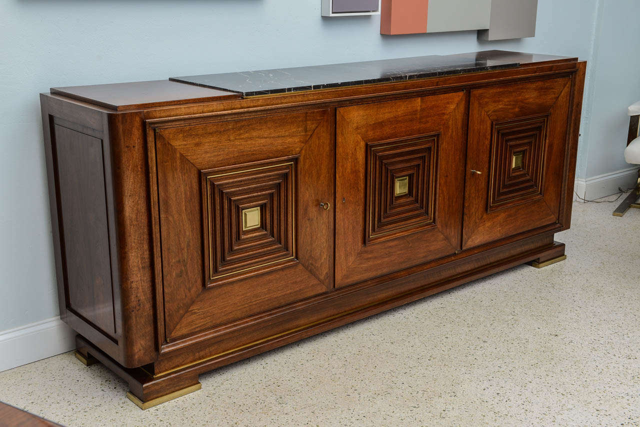 the inset marmo negro top flanking walnut reserves, over 3 paneled doors with raised squares, centered by a bronze center, on a plinth base, with bronze feet, illustrated in Maxime Old, Architect- Decorator, Yves Badetz, page 87, 1942