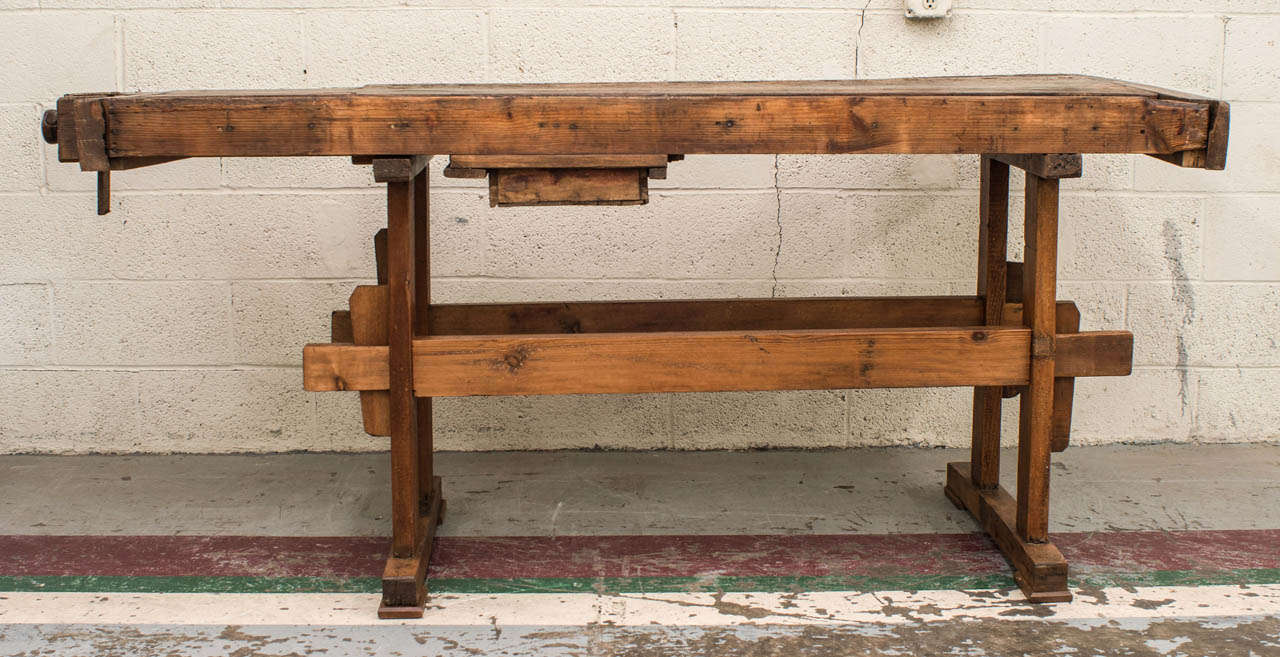 A handsome oak workbench on a collapsible oak and pitch pine trestle base with two stretchers with wooden keys.  The bench features two wooden screw-turned vises with exposed hand-cut dovetails.  The single hand-cut dovetailed drawer with original