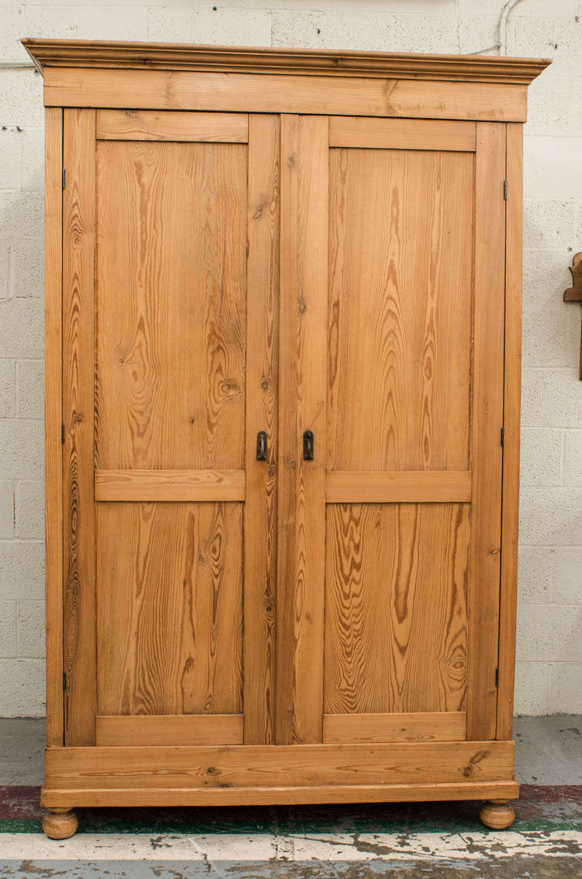 A plain, panelled, and spacious two door armoire which completely knocks down for ease in transport and installation.  Doors open 180 degrees to reveal nine modern adjustable shelves.  Exposed hand-cut dovetails to the crown and base.