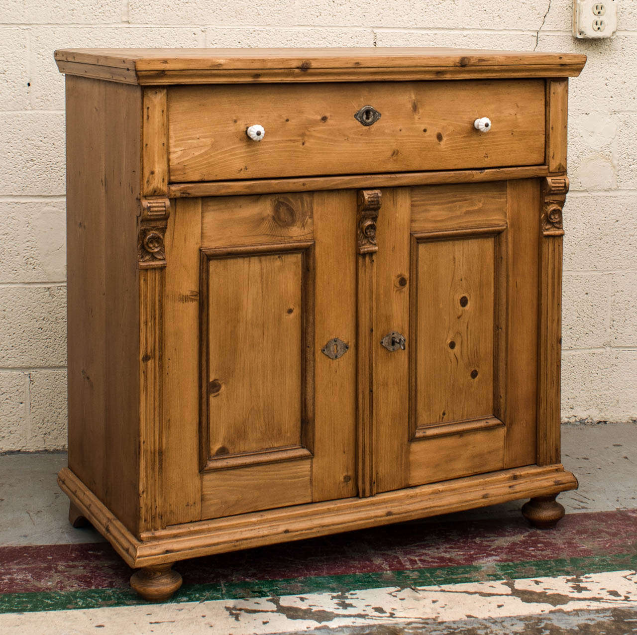 An attractive dresser base featuring a single hand-cut dovetailed drawer above two panelled doors, flanked and divided by fluted molding and unusual hand-carved floral corbels. Original ceramic pulls and nickel escutcheons.  Great as a compact