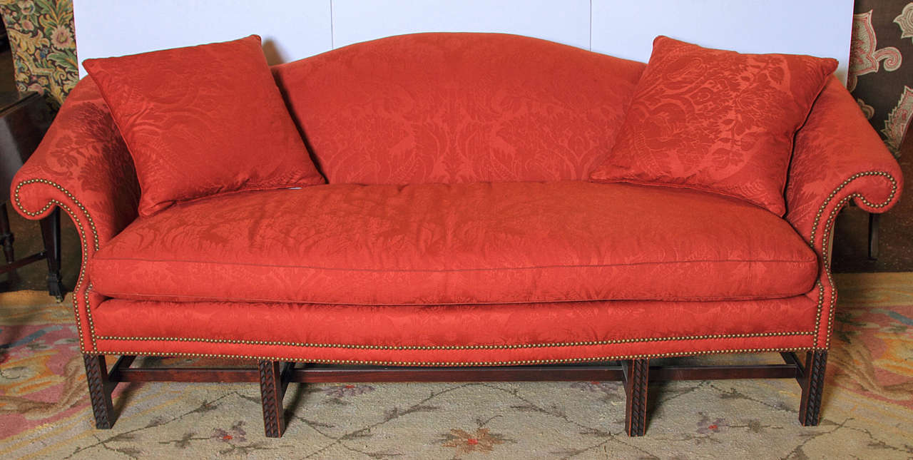 Early 20th century Chippendale style camel back sofa upholstered in red wool damask with nail-head trim.  (Re-furbished).  Front legs are carved.  Three pillows.