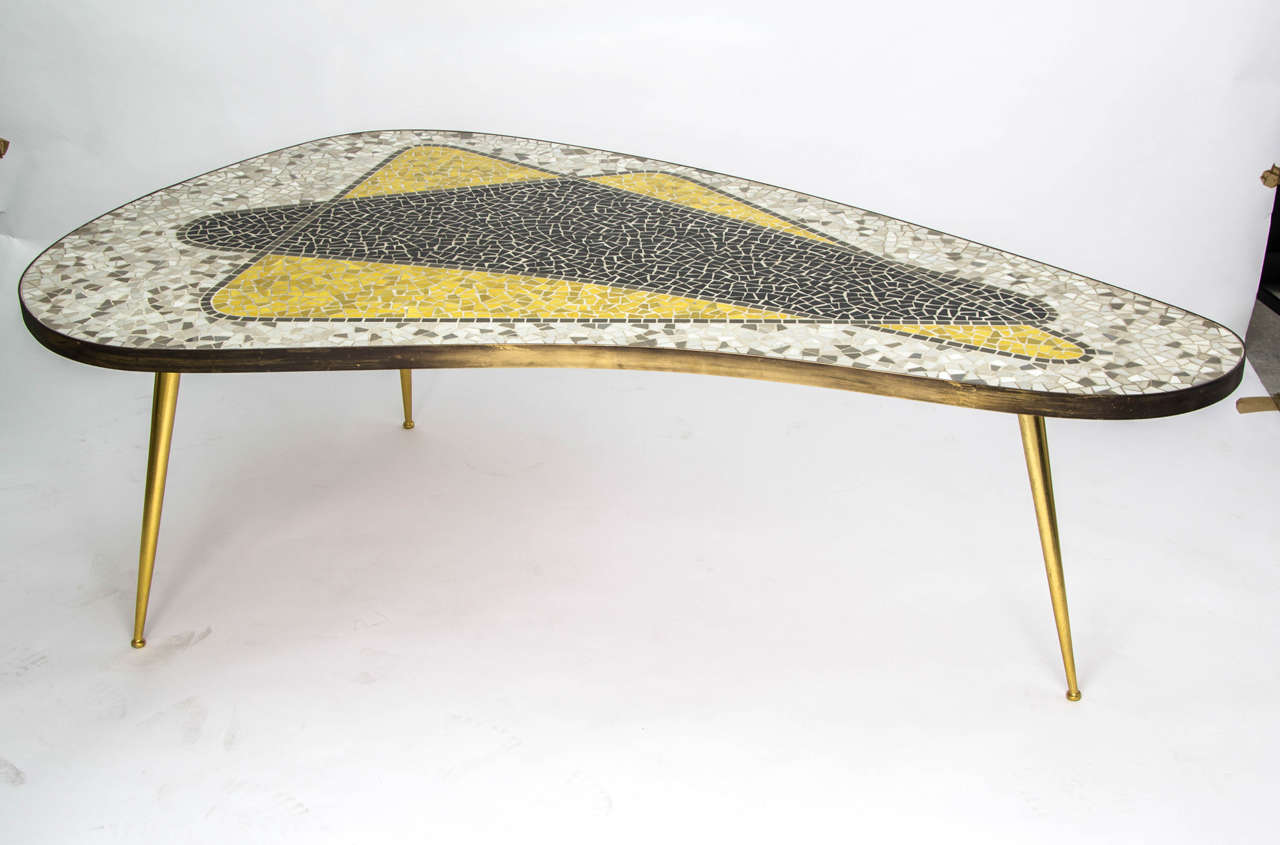 Mosaic kidney-shaped coffee table, or side table.  Germany 1950s.

The table has an atomic design in grey, brown, black and yellow stone.  It has a brass edge - with nice age-related patina - and three pointed legs.
