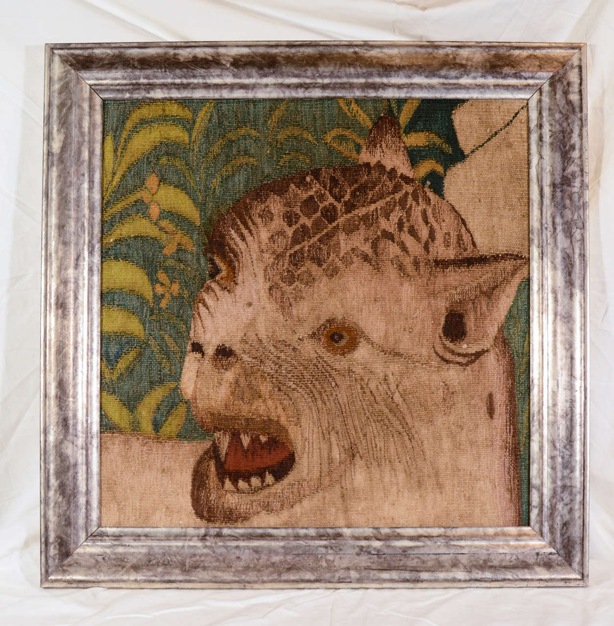 A framed wool tapestry showing a leopard, his fierce face turned towards us, his teeth bared as if some prey had caught his attention. 
This is a fragment of a larger tapestry. In the mid-18th century there were many tapestry workshops in France