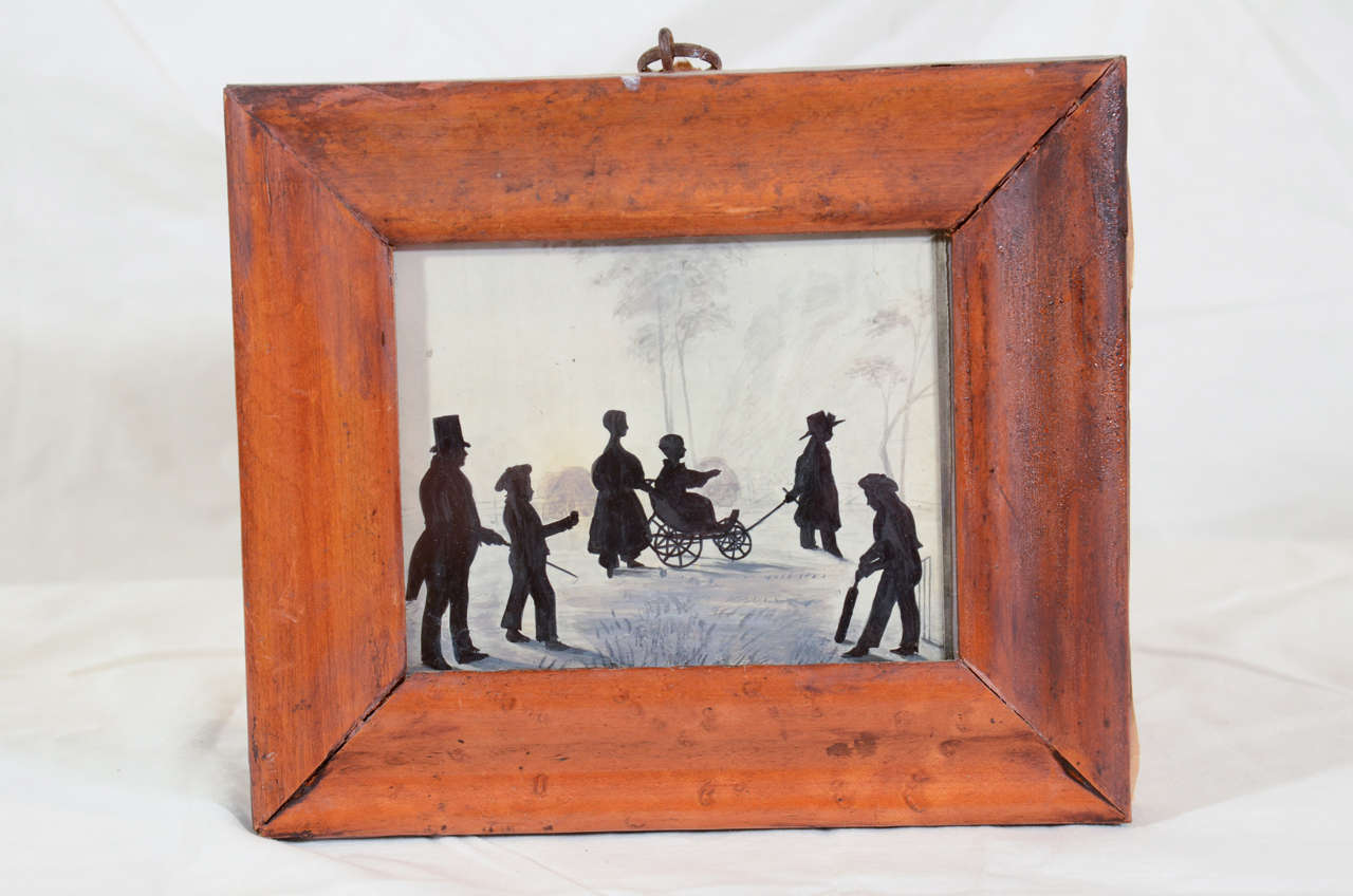 A charming painted silhouette of children at play: 2 boys playing cricket, and 2 older children pulling a younger child in a wagon, all chaperoned by their rather formal father wearing a top hat and tails.
In an original veneered bird's eye maple