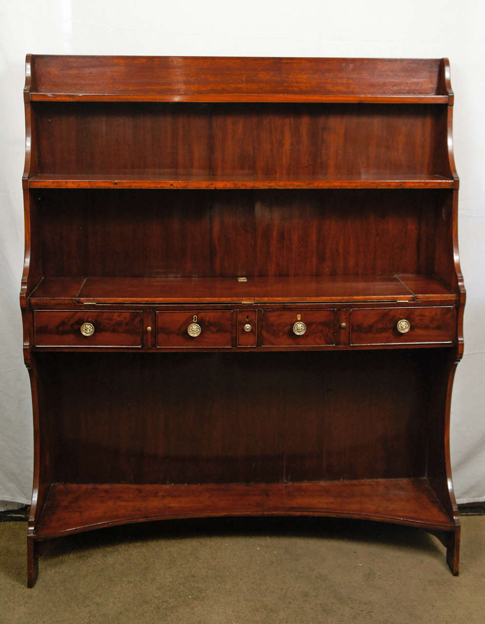 This finely made English regency period metamorphic bookcase-desk is also of an interesting and useful small scale. The mahogany construction is done in a clean simple straight-grained wood while the drawer fronts are enlivened with crotch mahogany