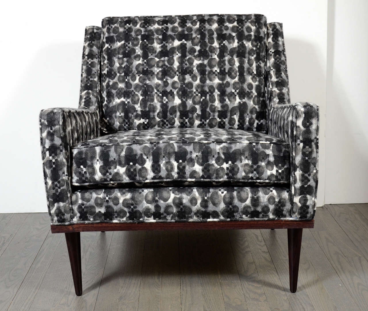 This chic Mid-Century armchair by Dunbar features a slender low arm, splayed conical legs in walnut  and walnut trim and has been newly upholstered in a very sophisticated black and white mottled  fabric.