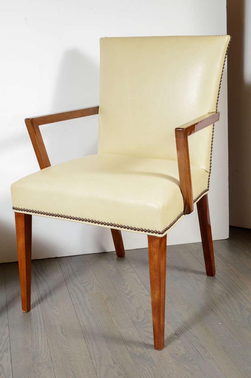 This pair sophisticated Modernist arm chairs in the manner of Robjohn-Gibbings feature antique brass nailhead detailing, elegantly tapered walnut legs and new ivory leather upholstery. With their angular arms offering a dynamic contrast to the