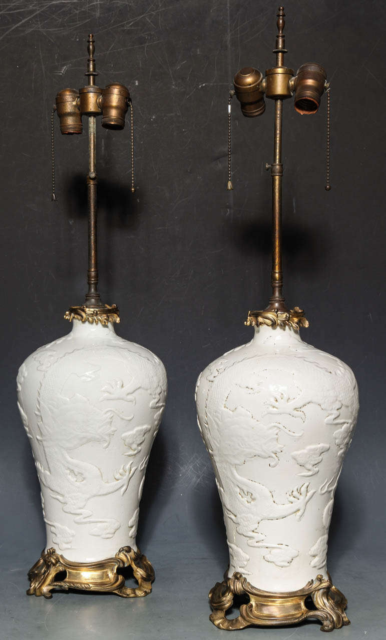 Paire de lampes de table en blanc de Chine et de style Louis XV français anciennement monté en bronze doré. La porcelaine est finement gravée à la main de motifs complexes de dragons et de nuages. Chinois, vers le 18e-19e siècle. Les montures en