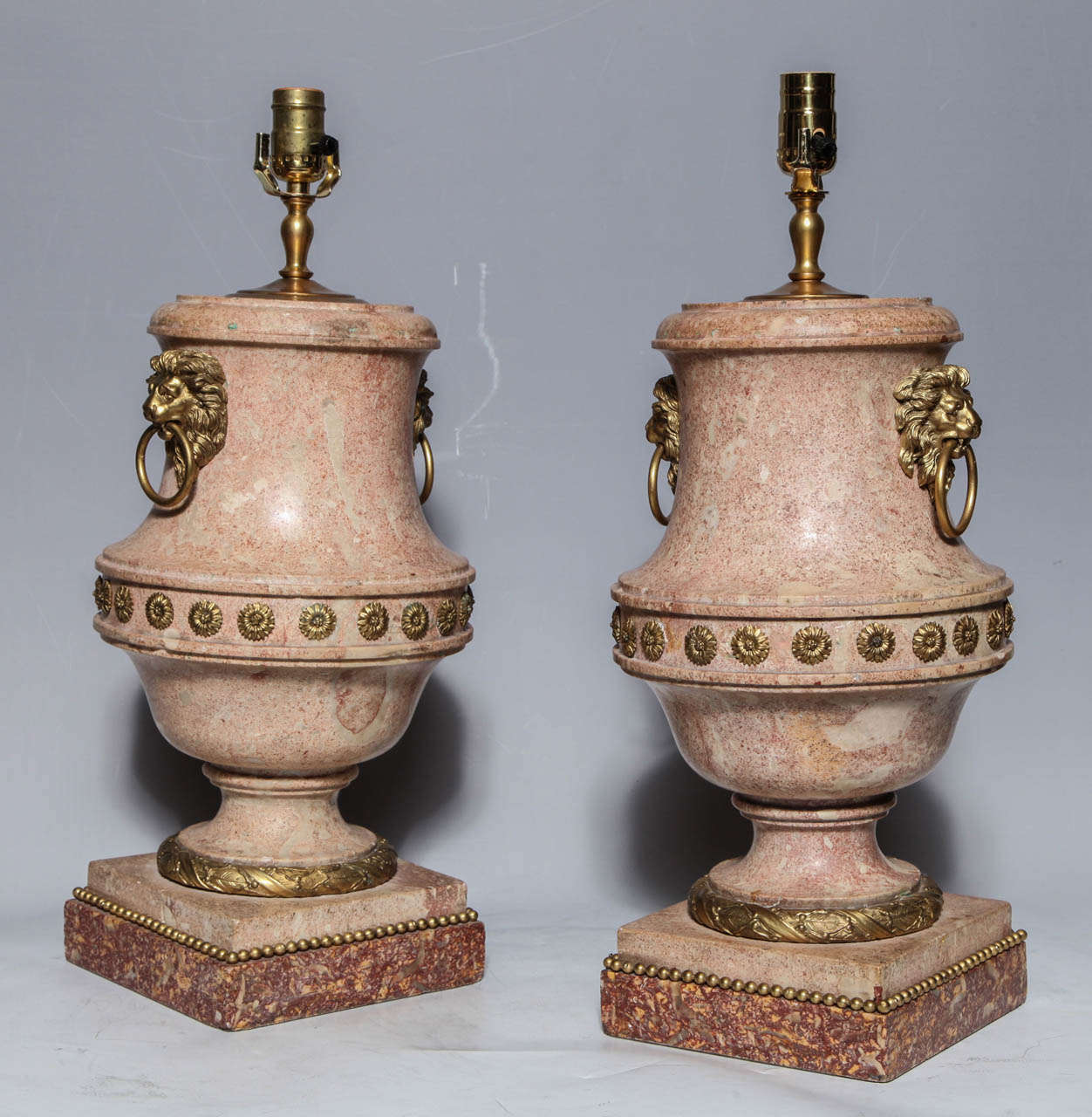 A Pair of Fine Quality Italian Scagliola Urns with Ormolu Mounts and Marble Bases, now wired as lamps. The lion mask bearing ring handles are well sculpted, as are the additional mounts.

Scagliola, is an art form devised as early as the Roman