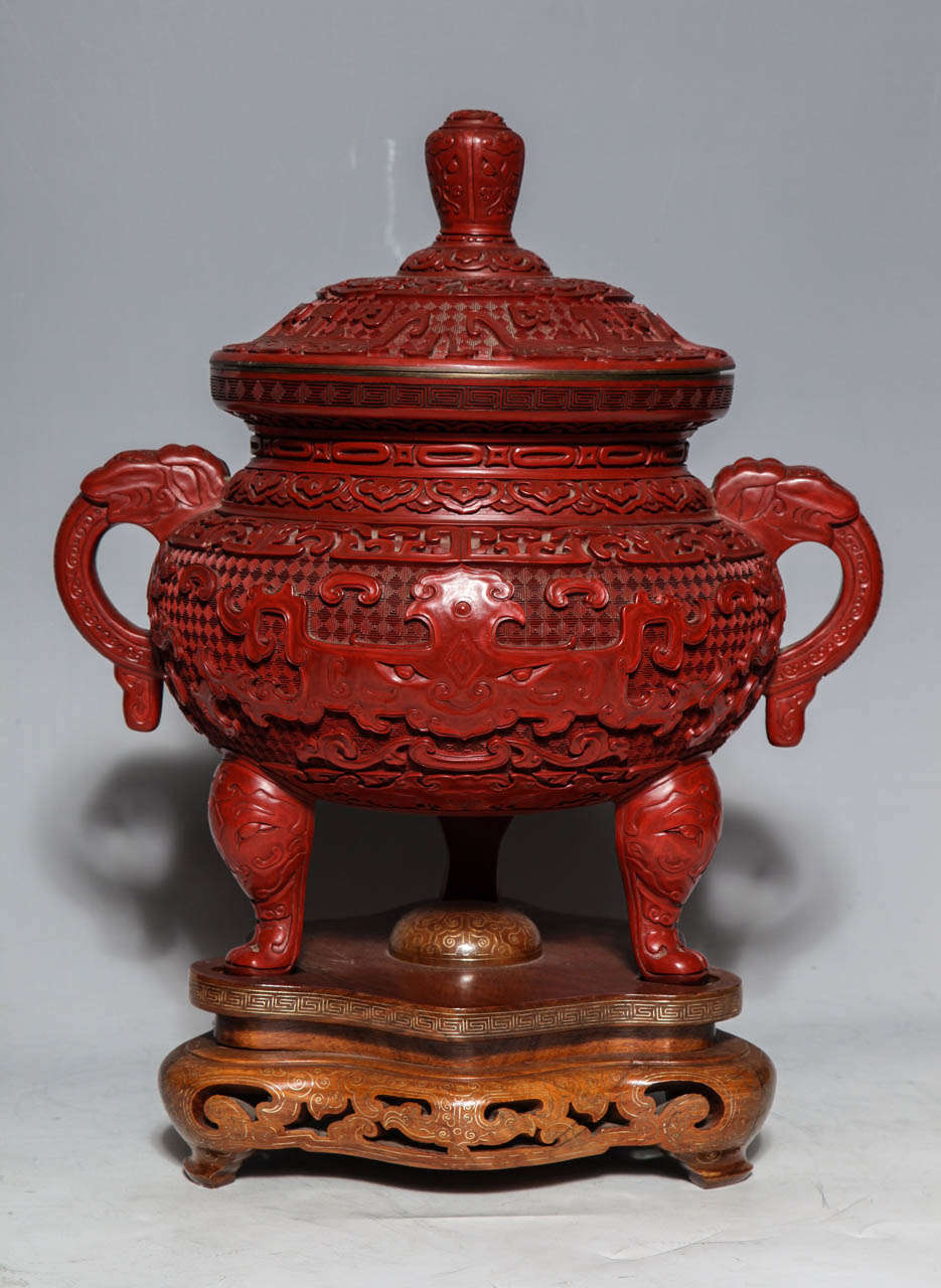 A Monumental Chinese Cinnabar Red Lacquer Incense Burner of Archaic Form and Decoration, with a conforming finely carved wooden base with Inlaid Silver. Intricate hand carved patterns show a dragon's face and serpentine handles. The belief that red