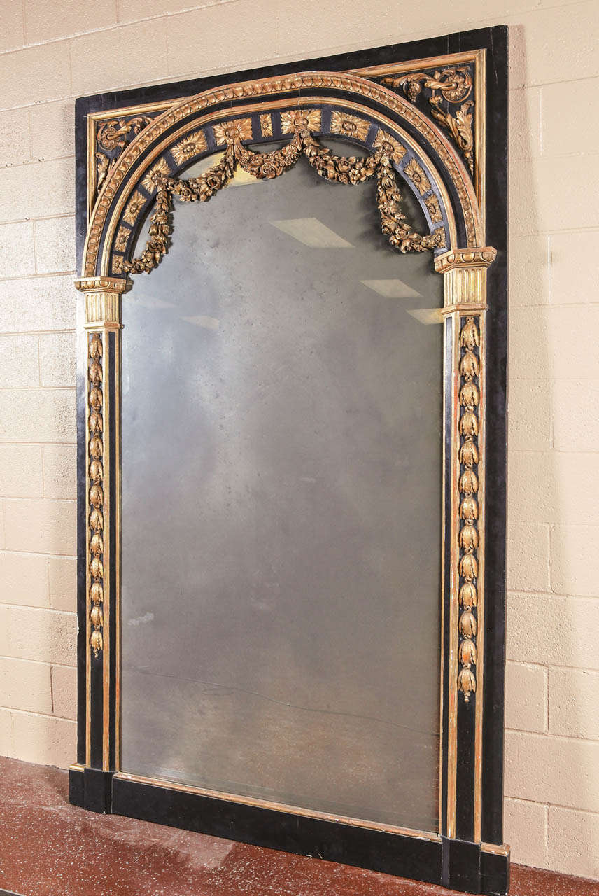 Large French Louis XVI style parcel gilt mirror with smoked glass.  Gilt highlights against a contrasting black ground with floral swags and the top. Circa 1900.