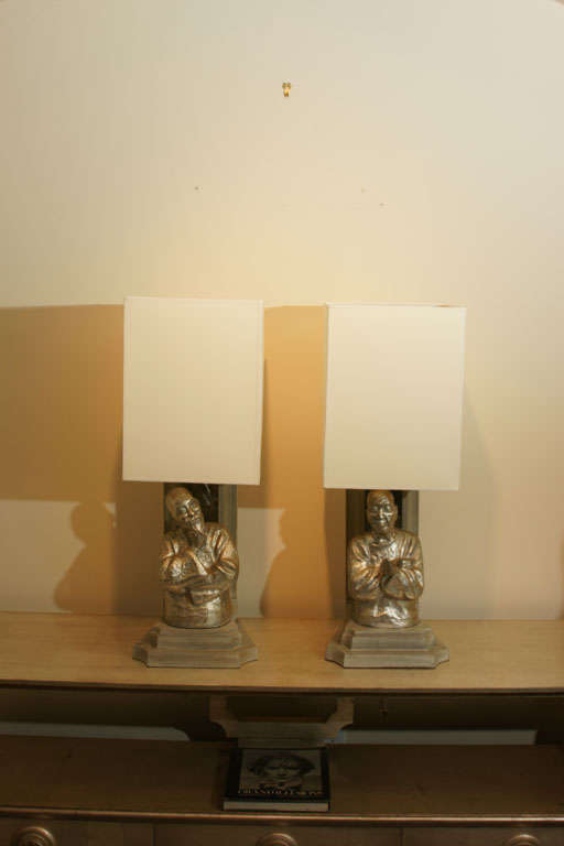 pair of wooden form pagoda lamps with carved figures by

JAMES MONT. The lamps tiered wooden back drops are a painted gray color with antique mirror, and the carved oriental statues are silver leafed. The lamps have been newly rewired have new