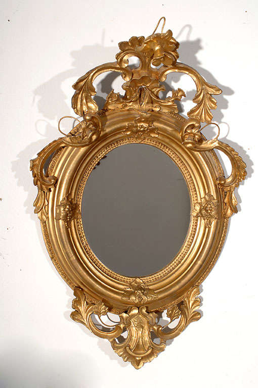 This charming oval mirror features foliate motifs with flowers blossoming at the ends of gilded wire stems. The crown and cartouche give it a real presence that belies its petite size.