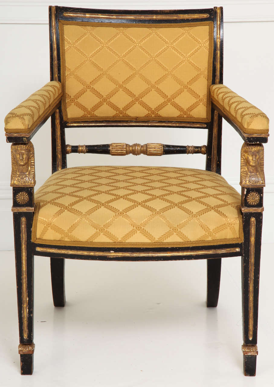 Regency black painted and parcel gilt upholstered open armchair, the padded square arms with carved Egyptian head supports continuing to tapering square front legs. The Battle of the Nile in 1798 resulted in the incorporation of Egyptian motifs into