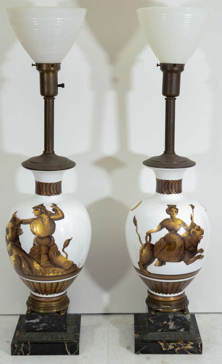 A pair of vintage Tommi Parzinger table lamps with bronze and marble bases with white glass bodies and gilt designs.  Each is decorated with a classical female figure riding a bull and a lion.