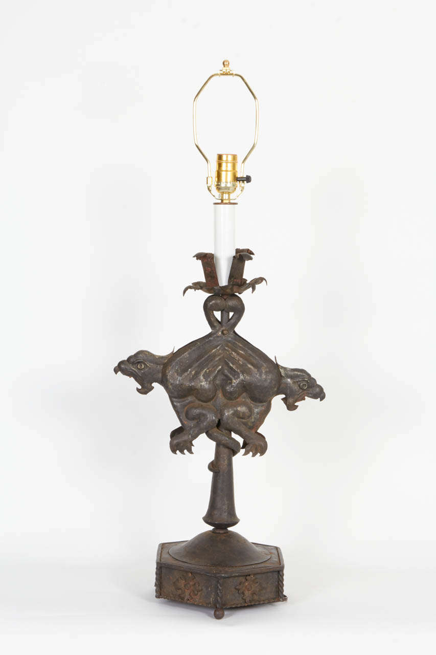 A pair of early 20th century Griffin lamps: each made with sheet metal (probably sheet iron) and black. The pair of outwardly twined griffins with mouths agape and talons grasping, the tails coiled around the lamp stems, raised on octagonal bases
