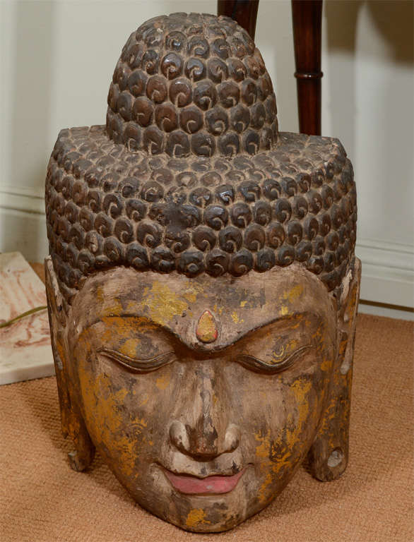 Impressive single block of wood sensitively carved into the image of Buddha.  Newly painted color tones and gold leafing highlight the face, bindi and elongated earlobes.  A mass of delicately carved curls are painted a deep brown.  Back of piece