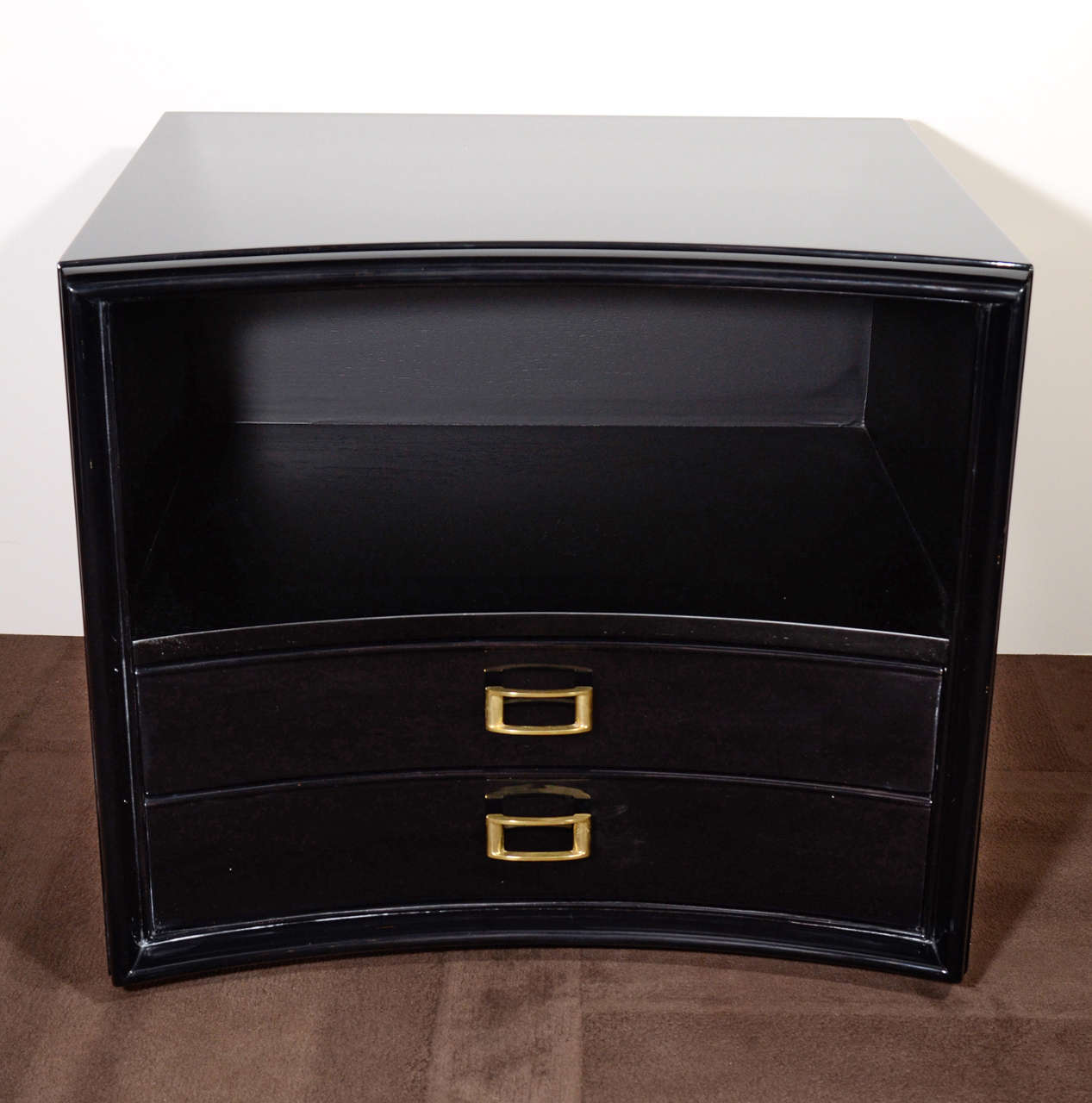 Exceptional end table or nightstand with modernist curved or bowed front. The table is conveniently fitted with two lower drawers as well as an upper open shelving or display area. Excellent design in ebonized walnut wood and with stylized brass