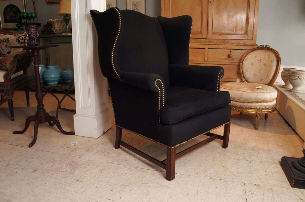Nicely upholstered black linen George III style wing back chair..  Brass nail head
decoration.   Loose cushion.   Mahogany stretcher base.