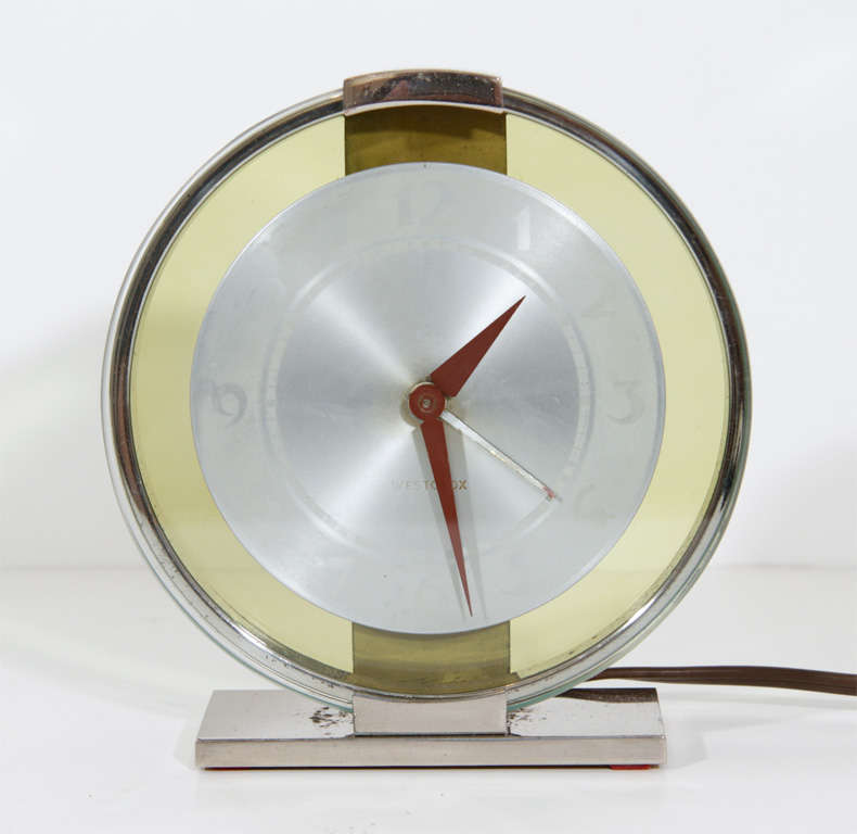 Art Deco Machine Age clock with aluminum dial plate contained within an amber glass surround bearing a chrome frame and base.