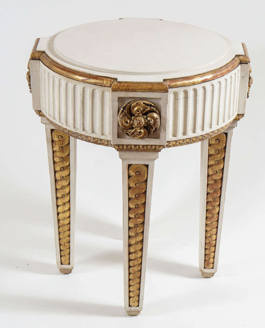 Exquisita gueridona o mesa auxiliar neoclásica francesa de época de Napoleón III, de roble macizo dorado y pintado, con tablero circular de frente quebrado con plinto central elevado sobre grueso delantal acanalado con rosetas talladas en