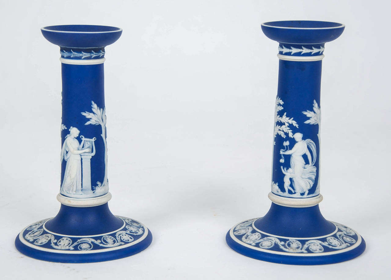 This is a fine early PAIR of JASPER WARE, stoneware, candlesticks in the rarer dark blue ground, made by WEDGWOOD, England in the mid 19th Century 

Each candlestick has a rounded cup socket, supported by a tapering cylindrical column moulded in