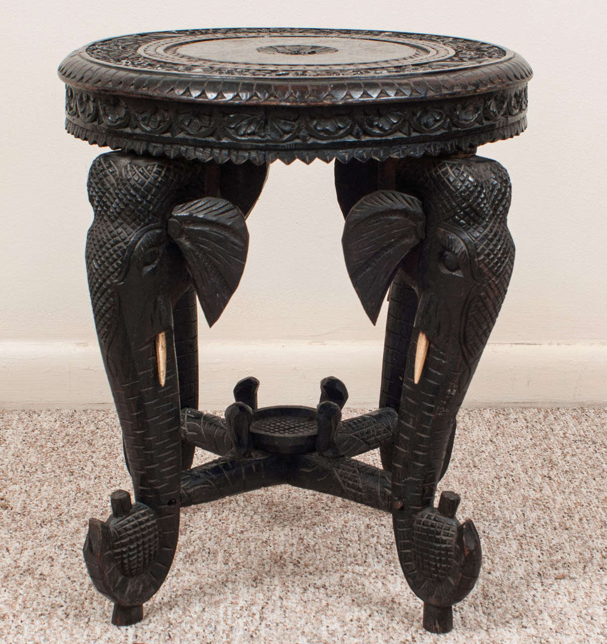 The round top supported by for elephant form legs joined by a stretcher centered by a platform for a vase or urn.