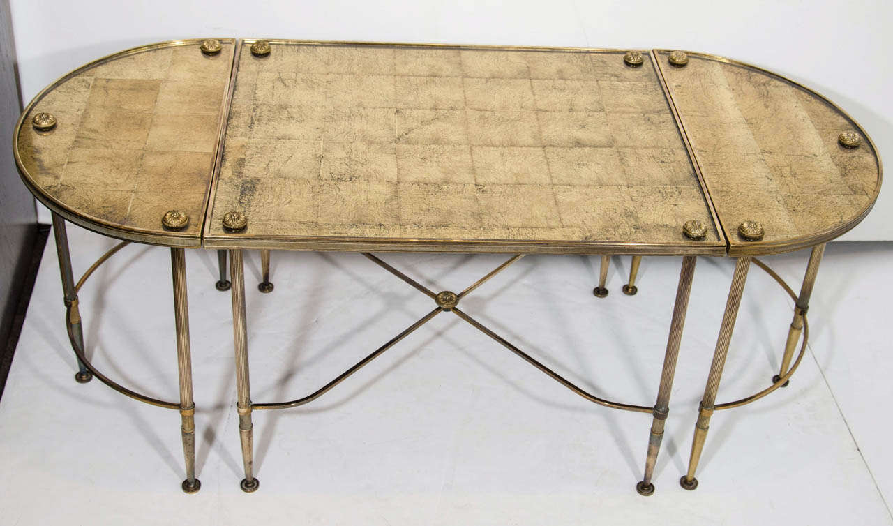 Elegant cocktail table set consisting of three parts. The tables have a directoire inspired design and feature eglomise (reverse painted) gilt leaf and glass tops with patinated dark brass frames. The center table has a rectangular top form, while