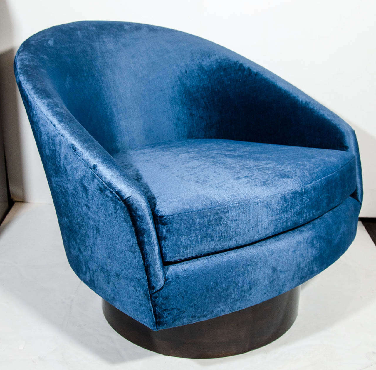 Outstanding pair of ultra modernist lounge chairs with swivel bases. The chairs have a deep barrel back design with inclined armrests. Newly upholstered in sapphire velvet by Kravet, and with circular walnut wood bases.  Beautiful from all angles.