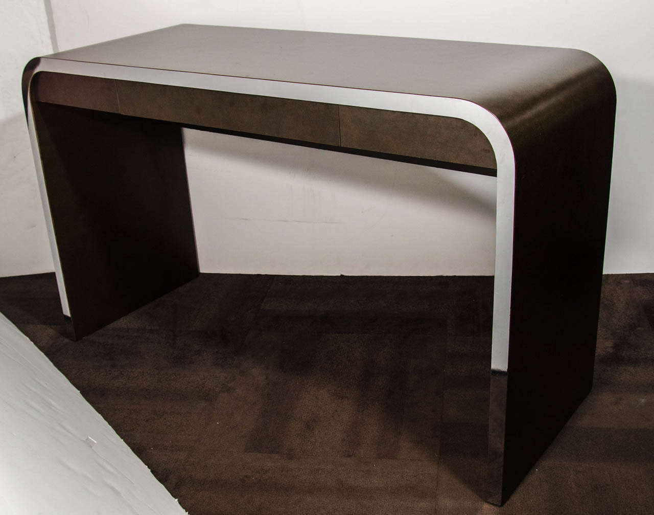Modernist writing table and console table in dark burled wood laminate with stylized chrome banded details. The table has a waterfall design with streamline curved edges, and is conveniently fitted with a narrow center drawer. The console is