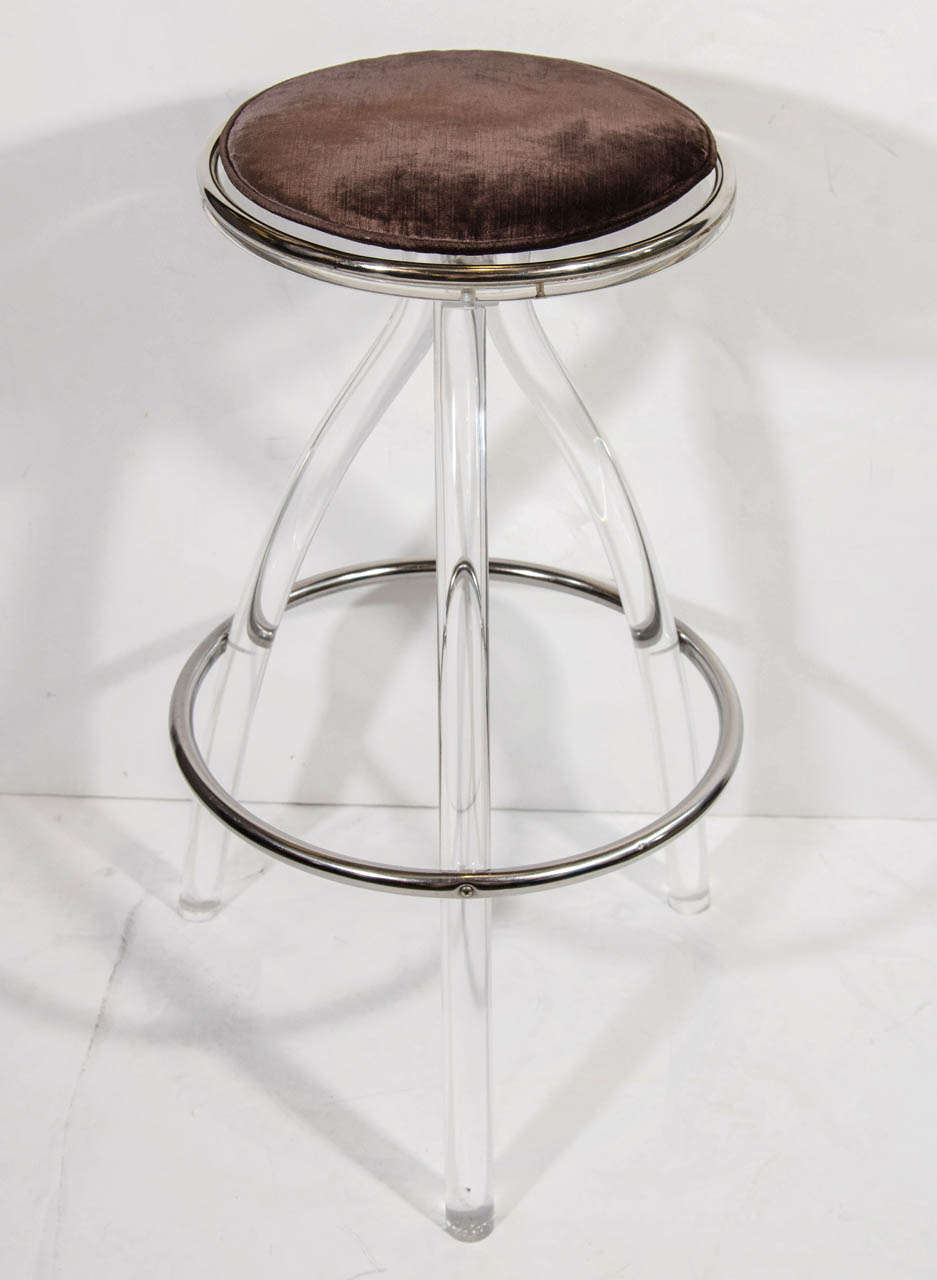 Pair of mid century modern bar stools in lucite. The stools have circular seats with chromed banded details. The stools have elegant scrolled bases with  tripod leg design and also feature circular chrome footrests. They work as counter stools and