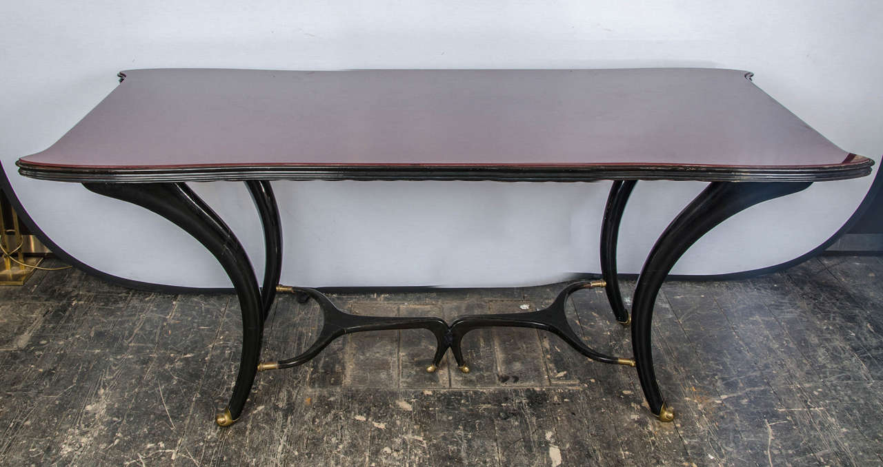 50's Italian dining table of organic form, in mahogany with red glass top and brass sabots