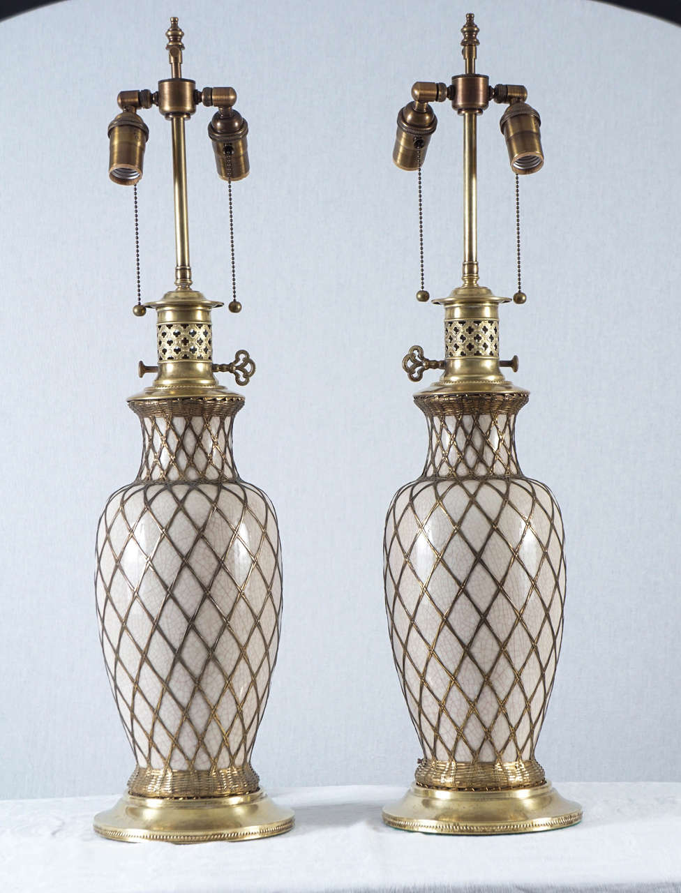 This very nice pair of creamy celadon porcelain lamps is French and mounted with brass tops and bases. The wire work that encases the lamp's is bright and very beautiful. While they look like oil lamp's they are currently wired for electricity.
