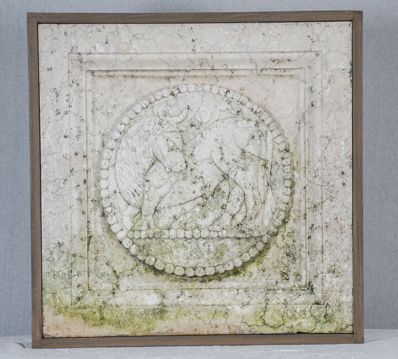 This carved marble plague is from a series representing the zodiac. Tarus is represented here as the bull looking back over his shoulder within a large  beeded border set further into a squared step framework. This piece by repute is from a