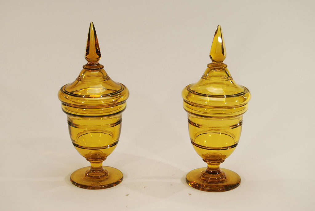 This is an impressive pair of Steuben Art Deco period covered vases with a clean architectural feel. Handblown crystal in a deep topaz/amber shade with simple radial cutting topped off with a facet-cut spire finial creates a dramatic statement, both